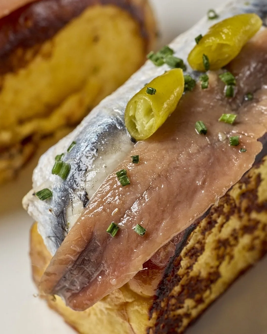 A toasted slice of bread topped with a cured anchovy and a pickled pepper