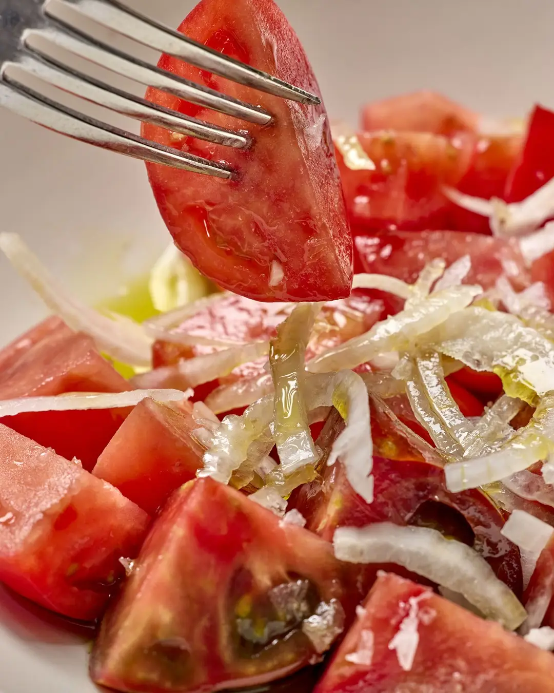 Close-up of tomato and onion salad with olive oil, fork lifting a tomato wedge