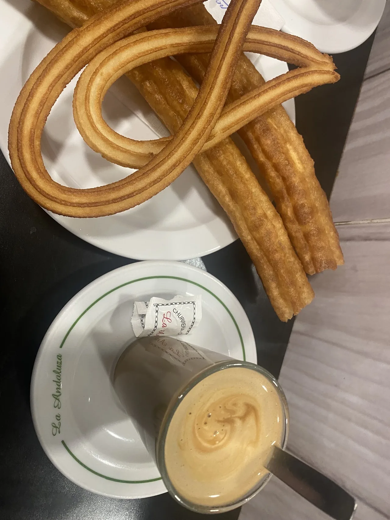Churros on a white plate seen from above beside a glass of coffee