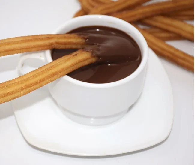 Churros dipped into a white cup of thick hot chocolate