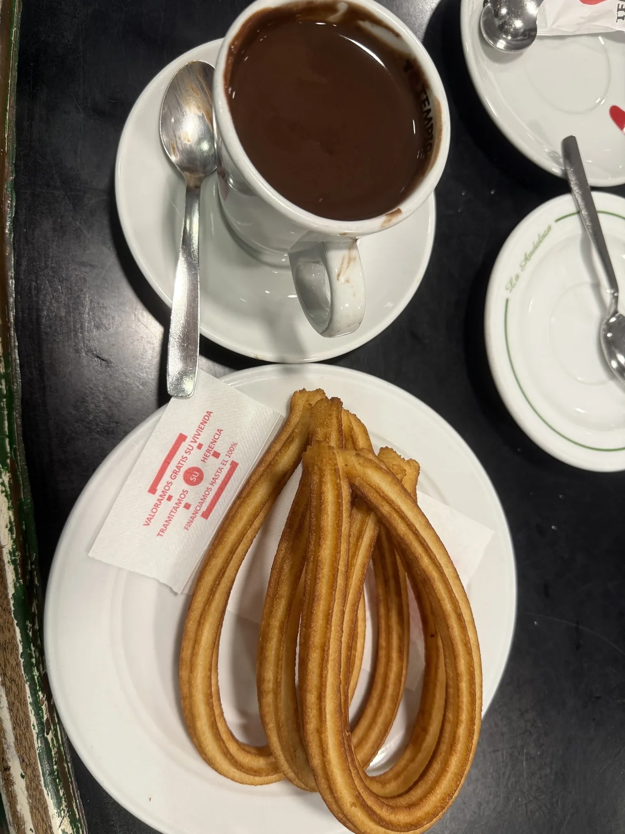 A plate of looped churros beside a cup of hot chocolate on a black table
