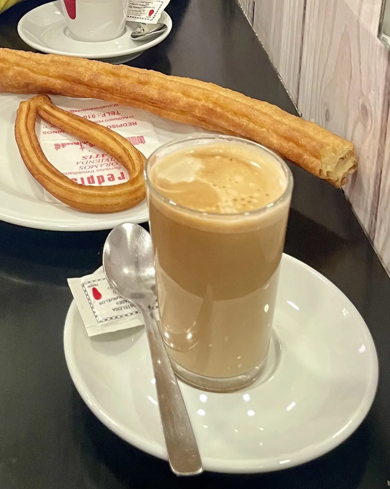 Looped and long churros on a plate beside a glass of café con leche