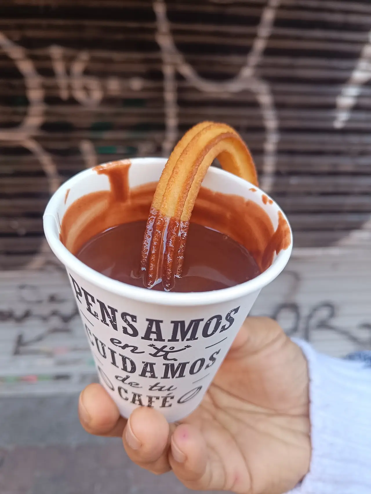 Churro dipped into a to-go cup of hot chocolate, held by hand