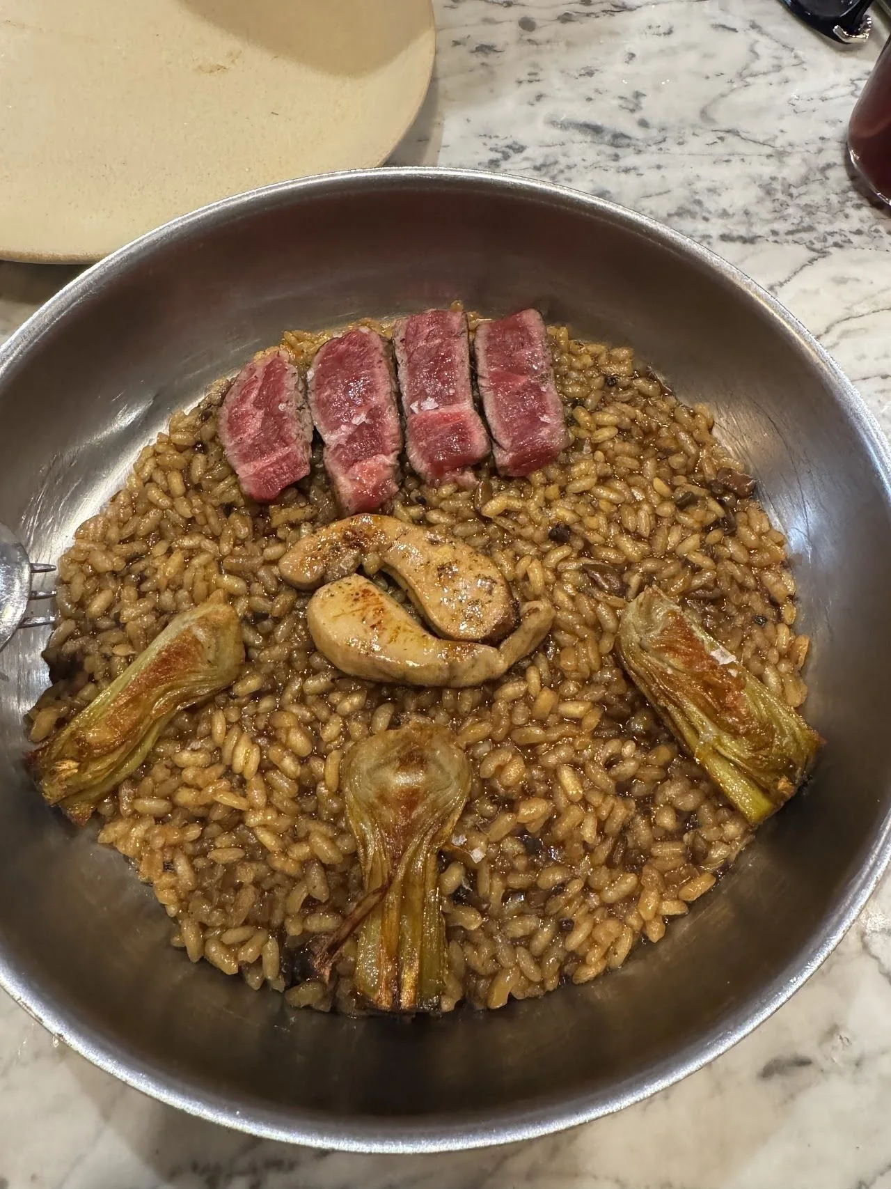 A metal pan of dark rice with seared red meat slices