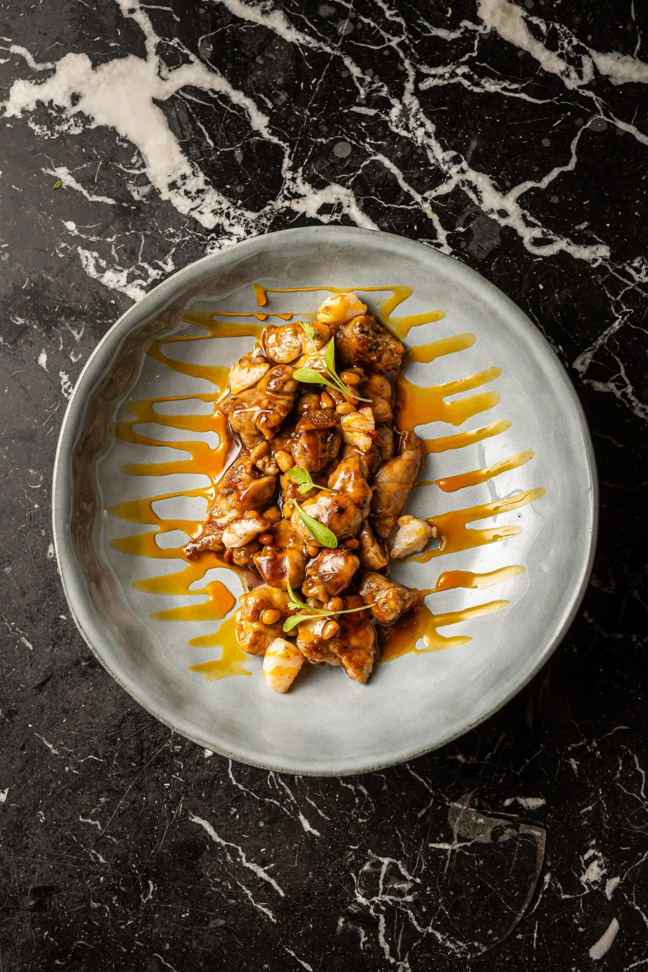 A grey plate of a brown sauced dish with orange drizzles on black marble