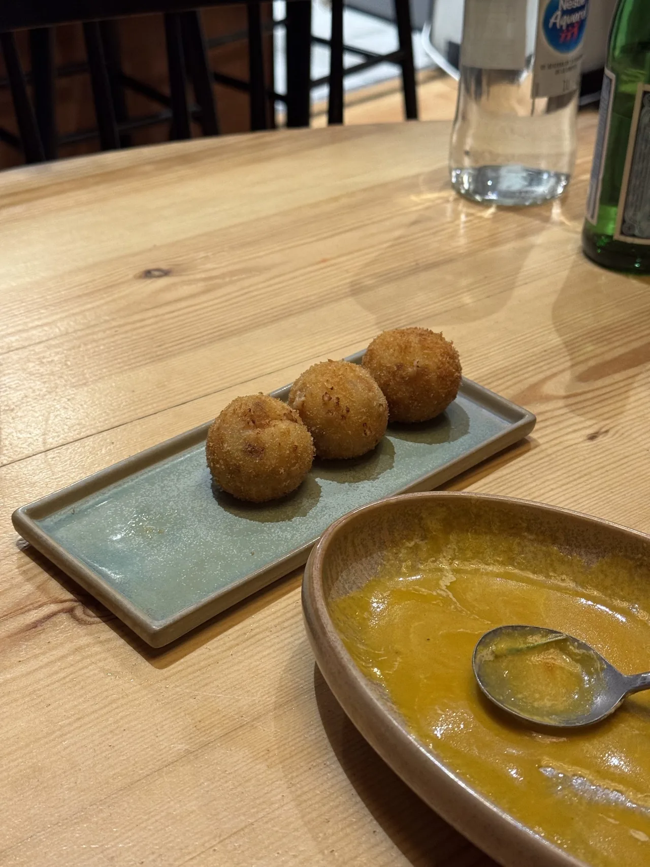 Three round breadcrumbed croquetas on a narrow blue-green tray on a wooden table
