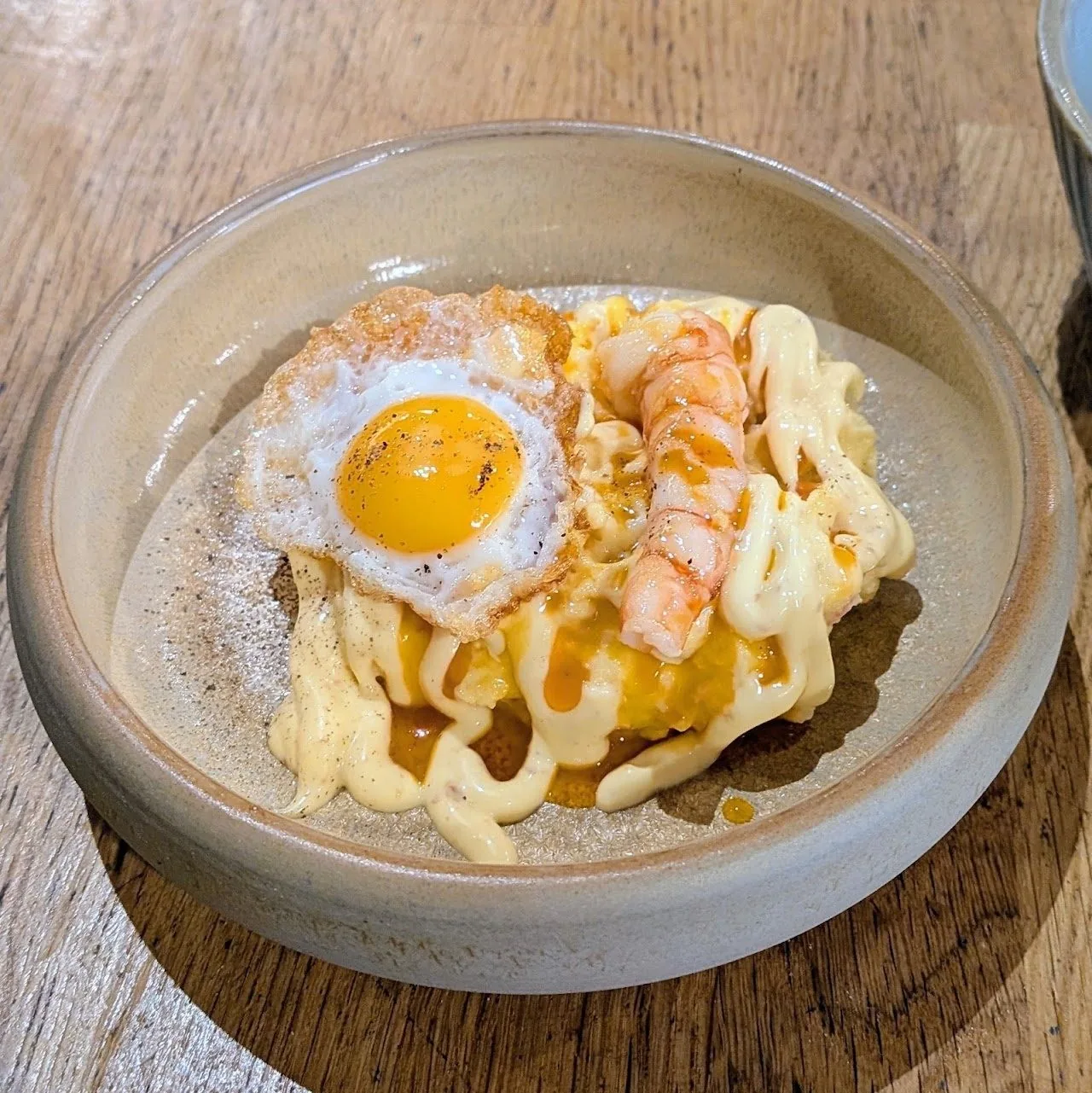A shallow bowl of pasta topped with a fried egg and prawns