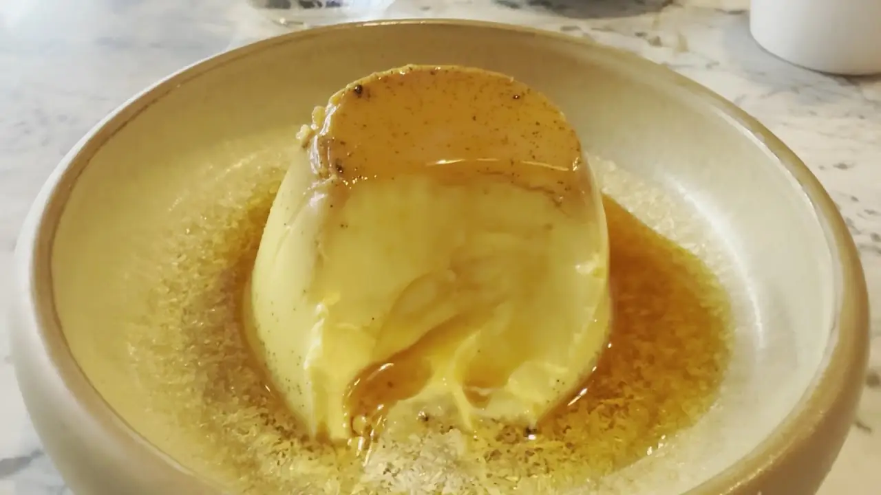 A caramel flan turned out onto a plate, with sauce pooling around it.