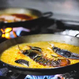 Seafood paella with lobster cooking over an open flame in the pan