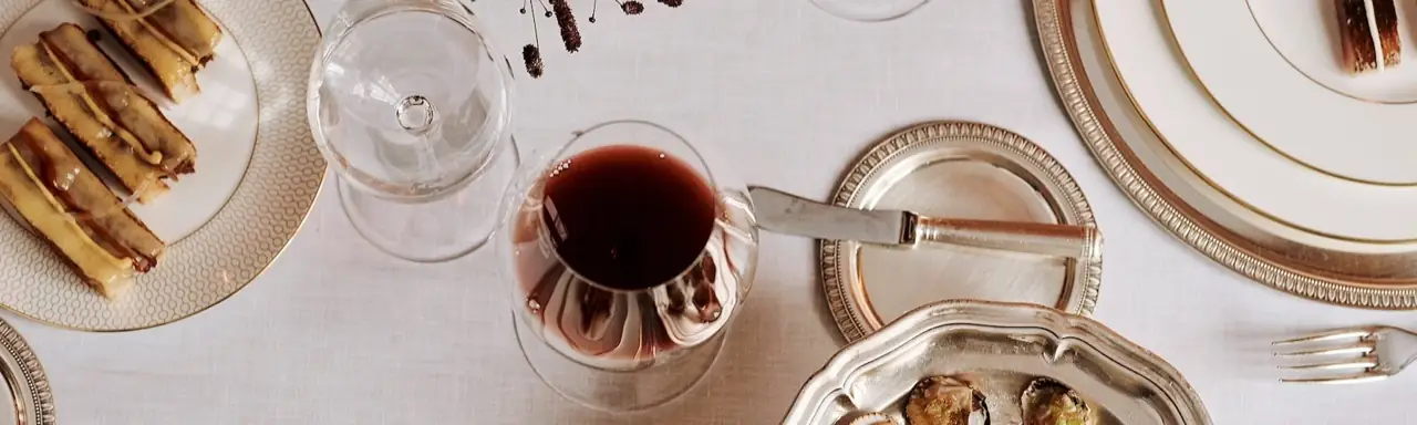 Overhead fine-dining table with a glass of red wine, silver plates, canelones and oysters on white linen