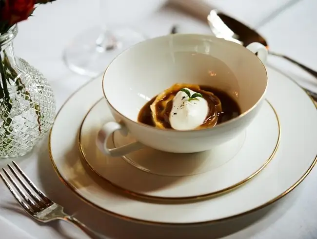 Consomme with a quenelle and herb garnish in a gold-rimmed cup on a matching saucer