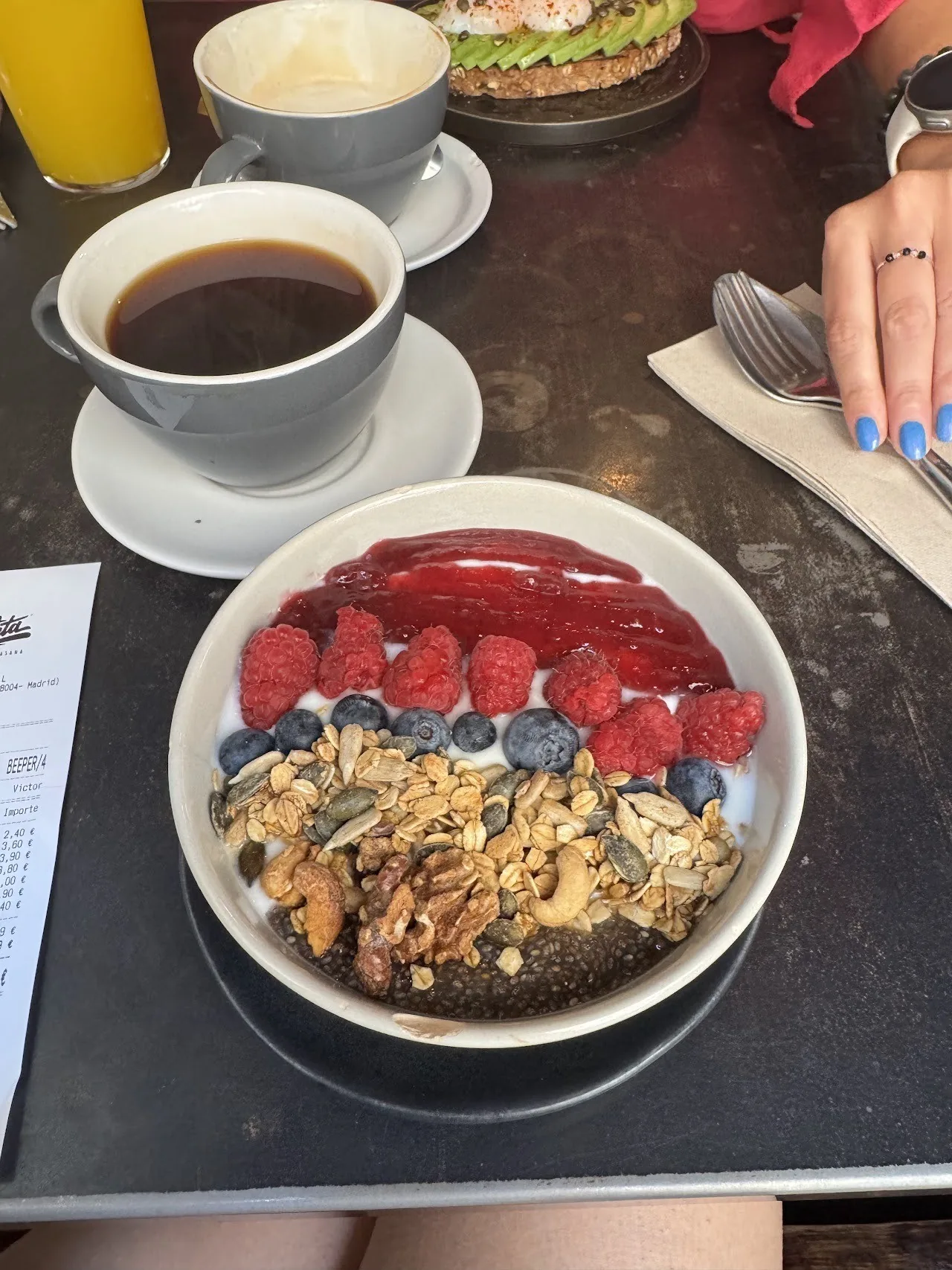 A bowl of granola, berries and yoghurt beside a cup of black coffee
