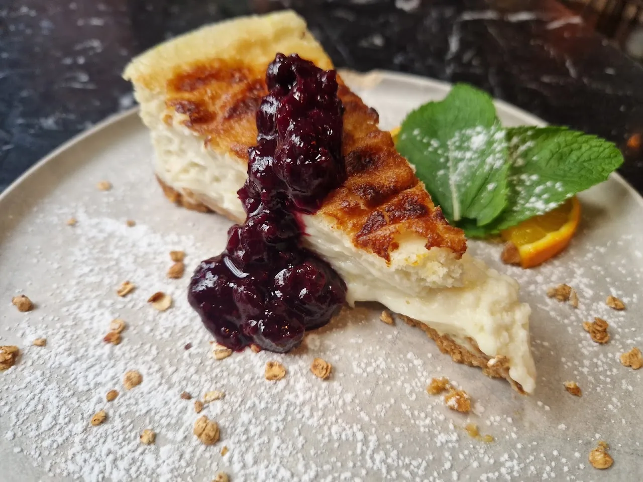 A slice of baked cheesecake topped with berry compote and mint