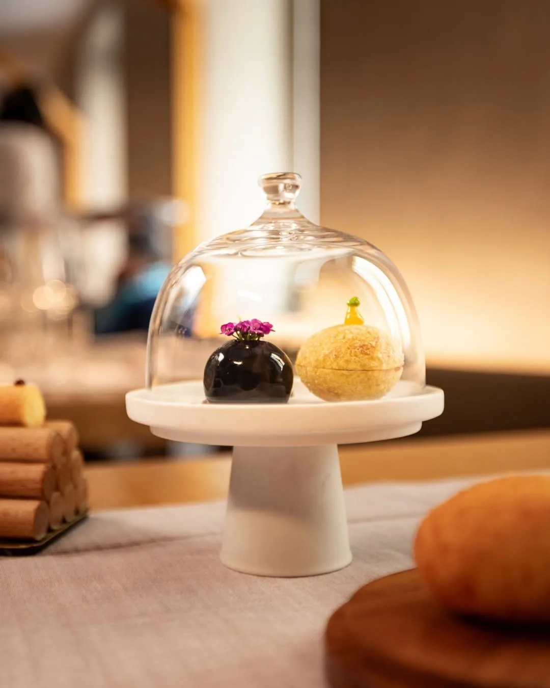 A glass dome on a white stand covering two small desserts
