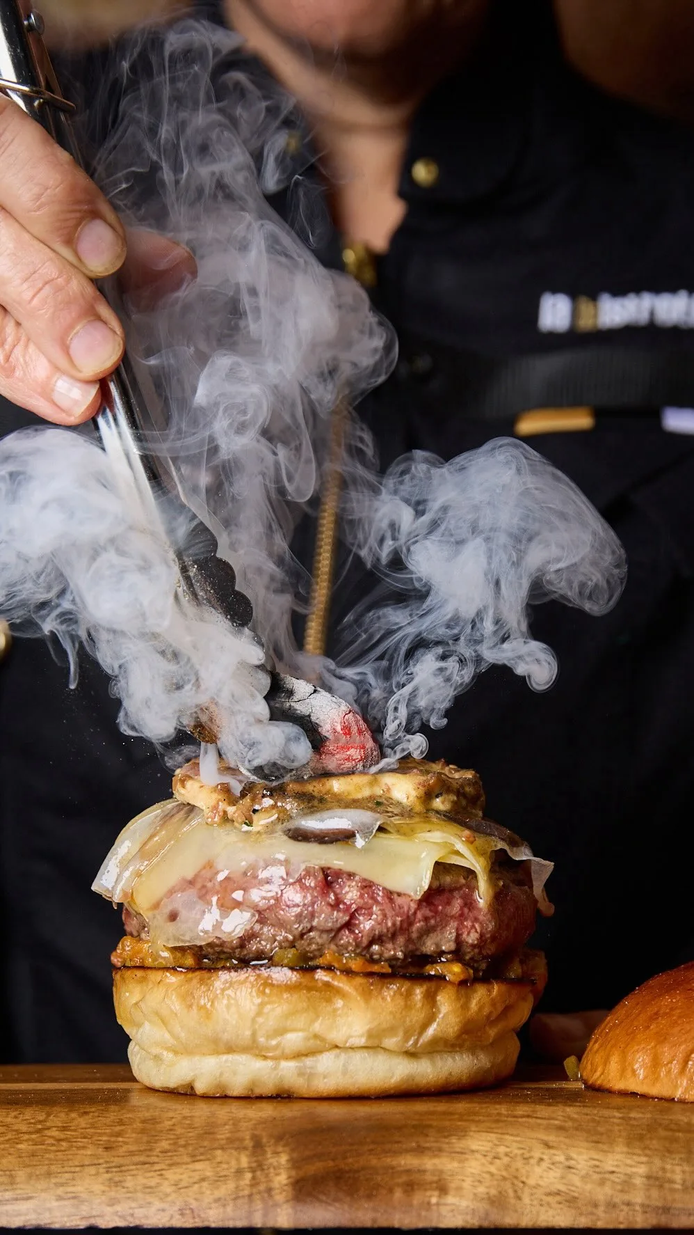 Burger being torched tableside with smoke rising from the bun