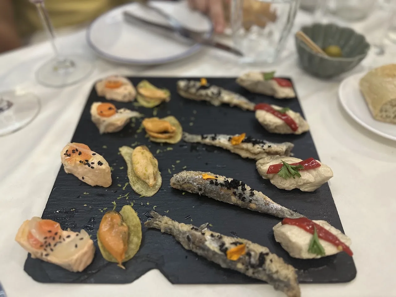 A slate board of assorted tapas including mussels and canapes with sauce dots
