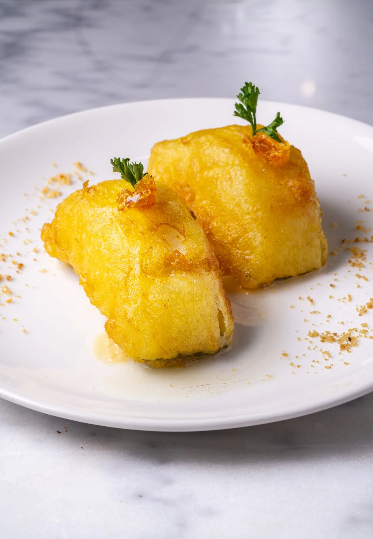 Two golden fried cubes garnished with herbs on a white plate
