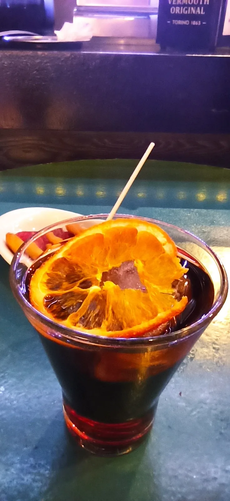 A red cocktail garnished with a dehydrated orange slice