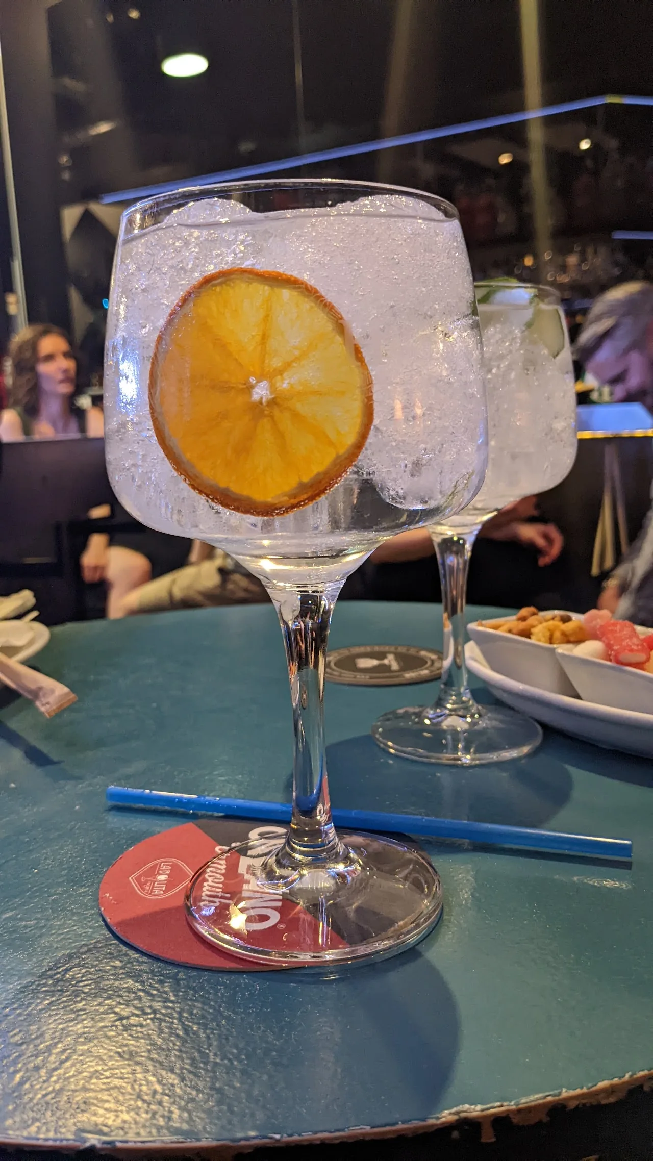 A gin and tonic in a balloon glass garnished with a large ice cube and orange