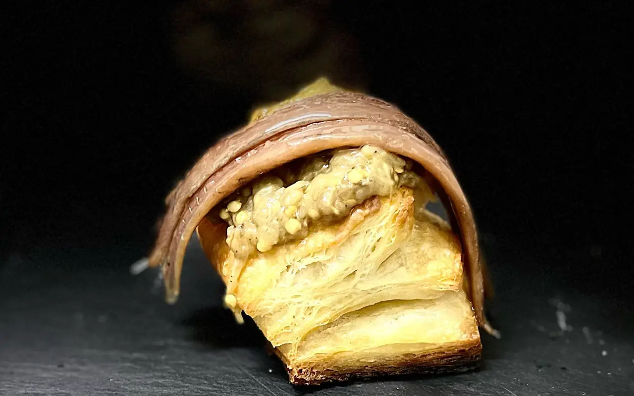 Anchovy fillets laid over a rectangle of layered puff pastry spread with a chunky pale-green sauce, on a dark surface.