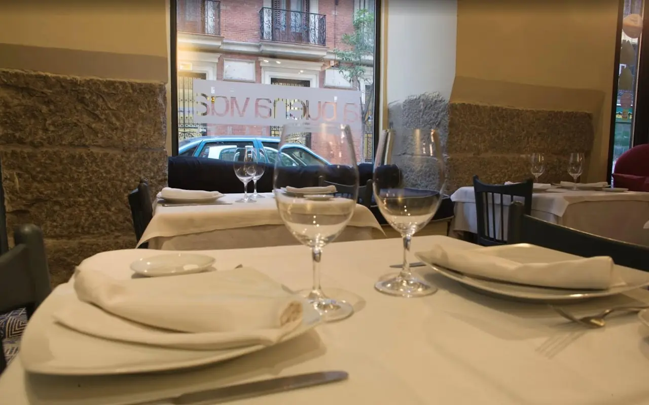 Dining room tables laid with white cloths and wine glasses, the restaurant's window lettering readable in reverse against the street outside.