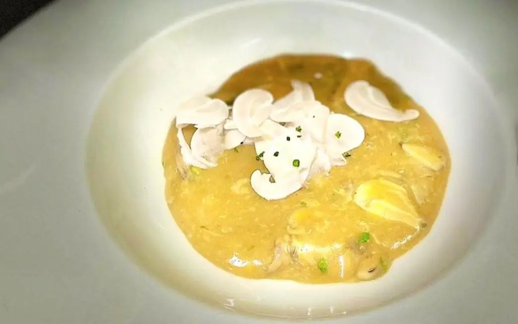 Shallow bowl of thick golden stew topped with raw sliced mushrooms and chopped chives.