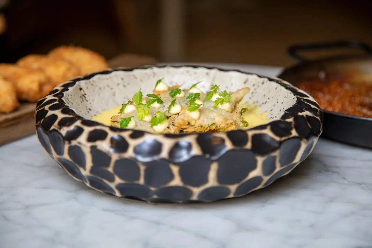 A patterned bowl of a creamy dish topped with green garnish on a white marble table