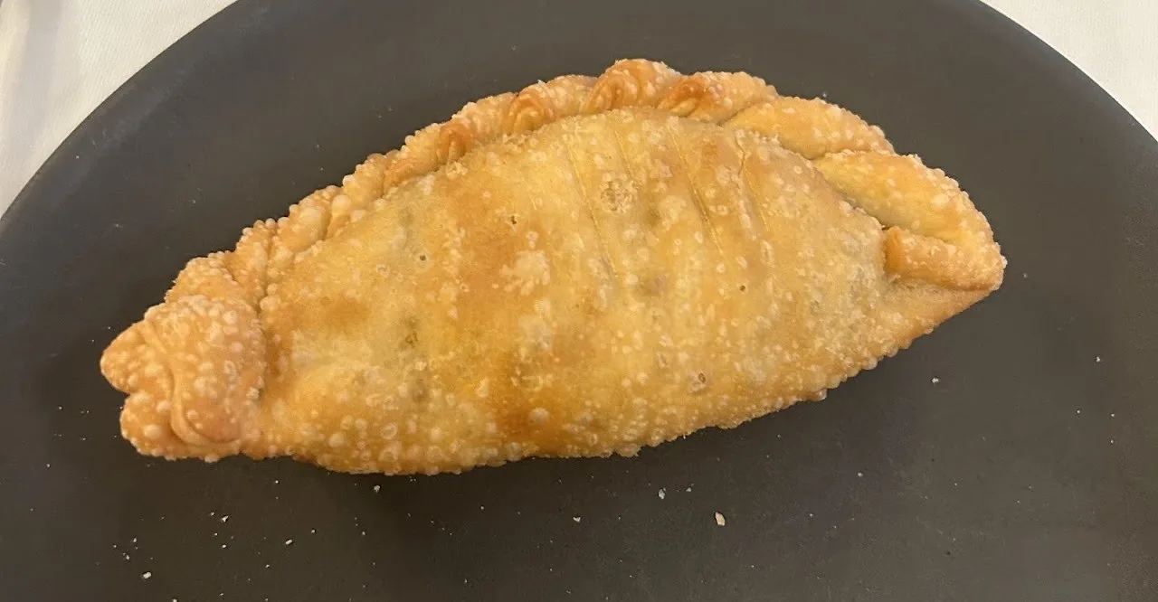 A golden baked empanada on a dark plate