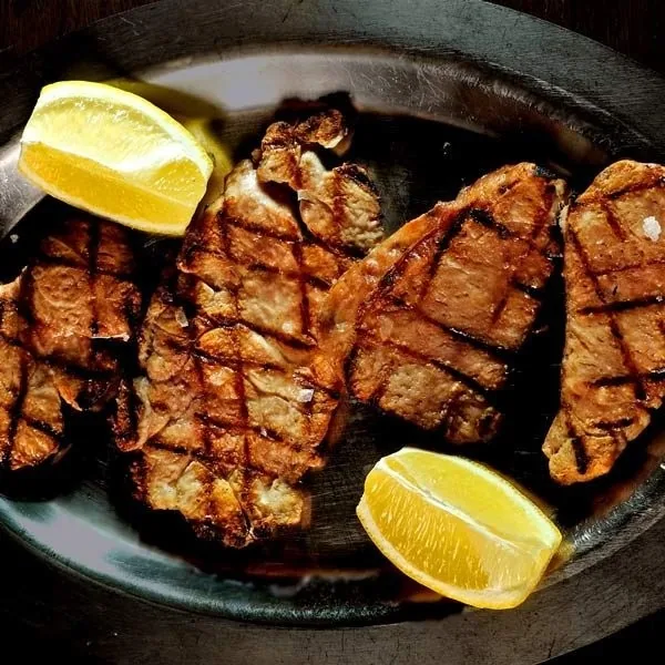 Grilled meat cuts with lemon wedges on a dark plate
