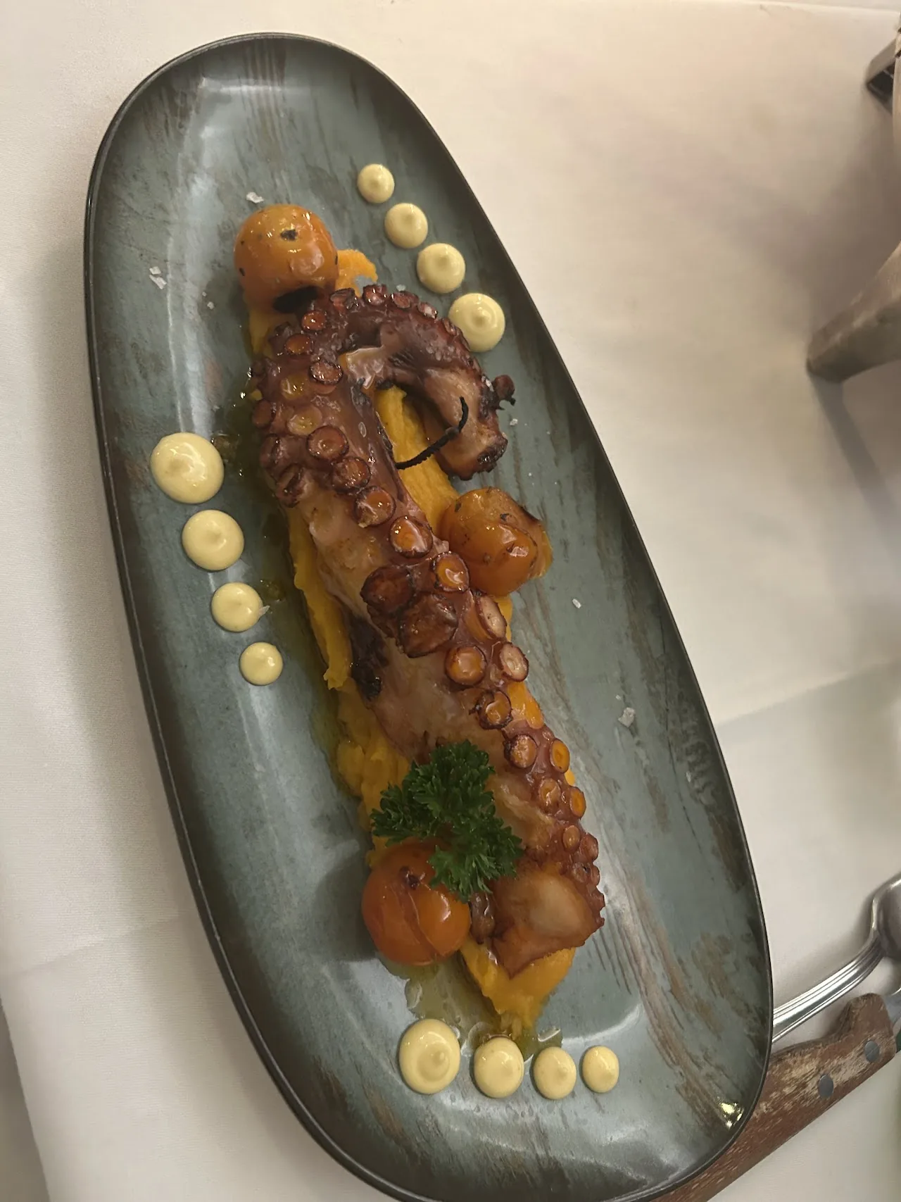 Grilled octopus on a plate with sauce dots and citrus wedges