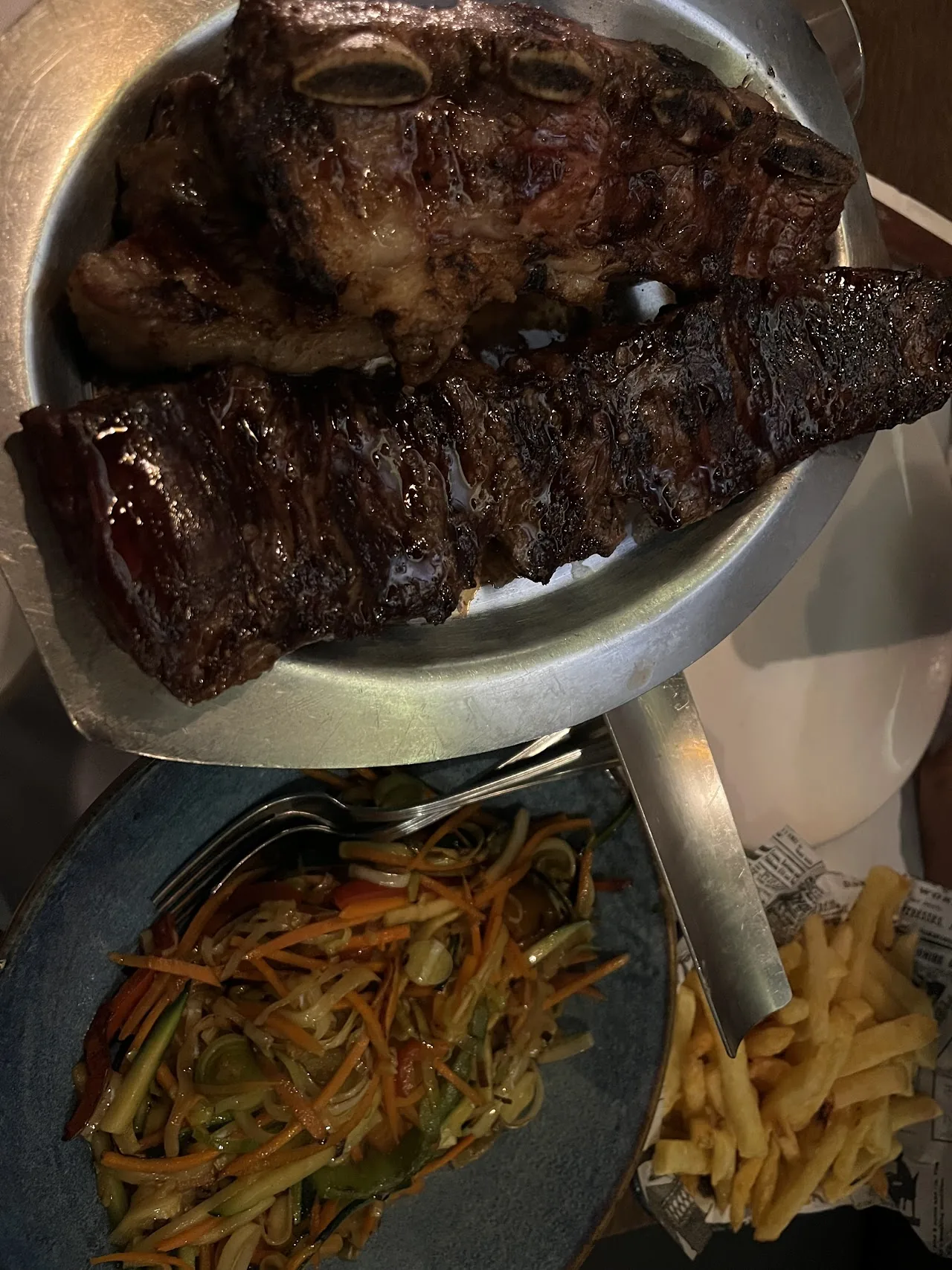 A grilled steak in a sizzling pan with a side of fries and vegetables