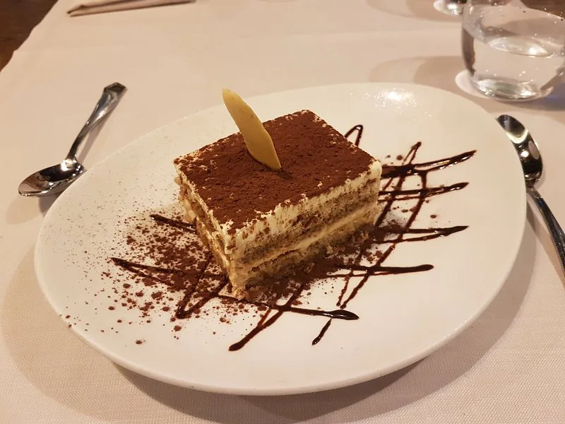 A slice of tiramisu drizzled with chocolate on a plate
