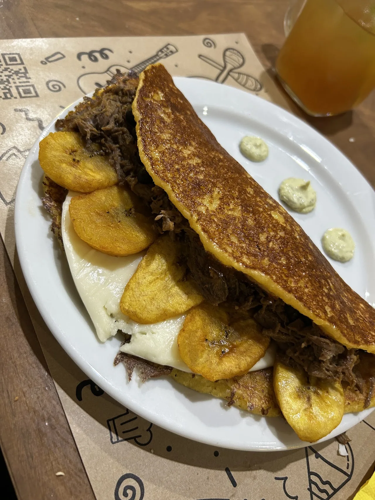 A folded cachapa (corn pancake) filled with pulled meat, served with fried plantains and cheese