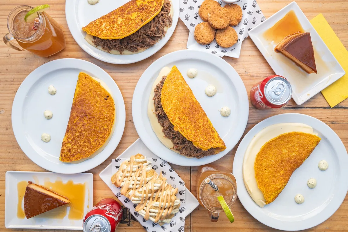 Overhead view of a table spread with folded cachapas, a slice of cake, and empanadas