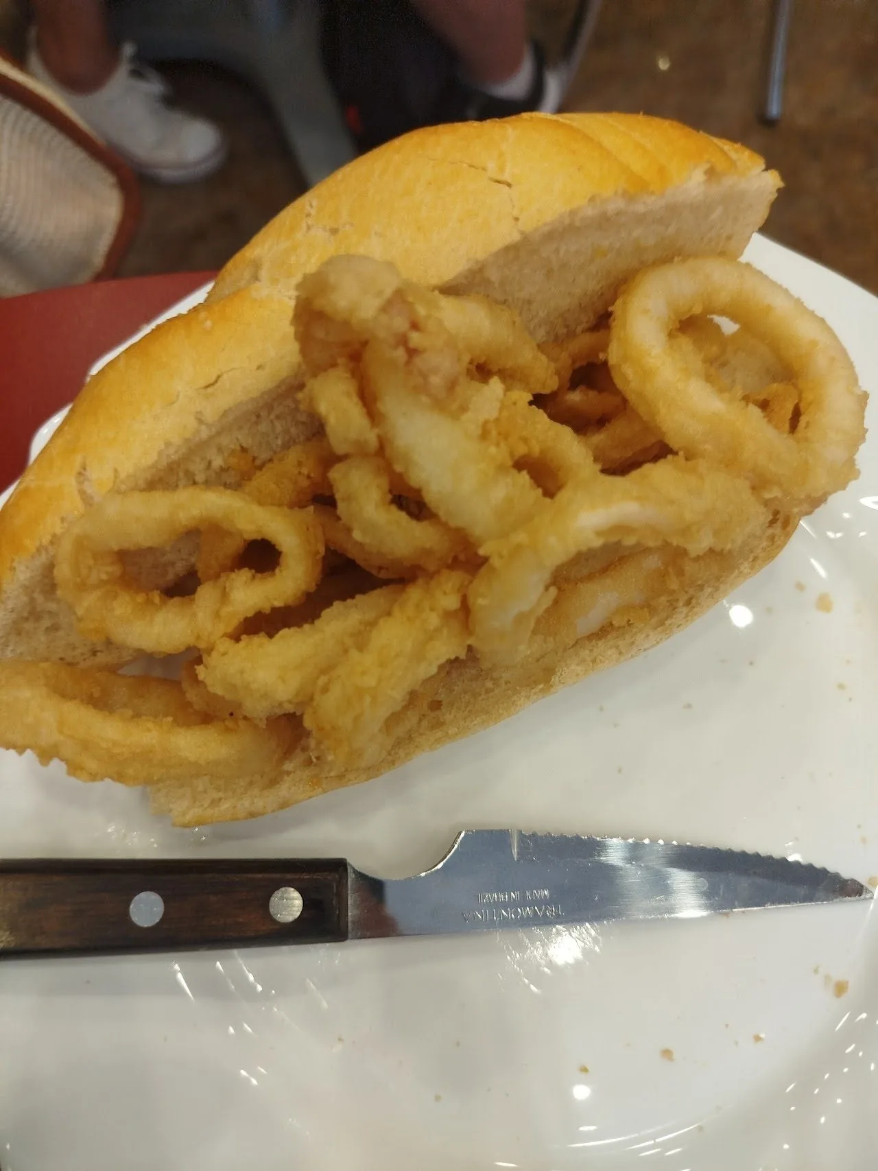 A fried squid sandwich on a plate with a knife beside it