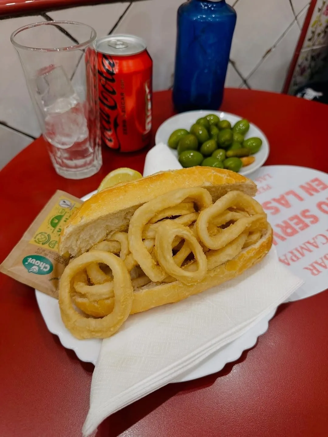 A fried squid sandwich on a paper napkin beside a bowl of olives