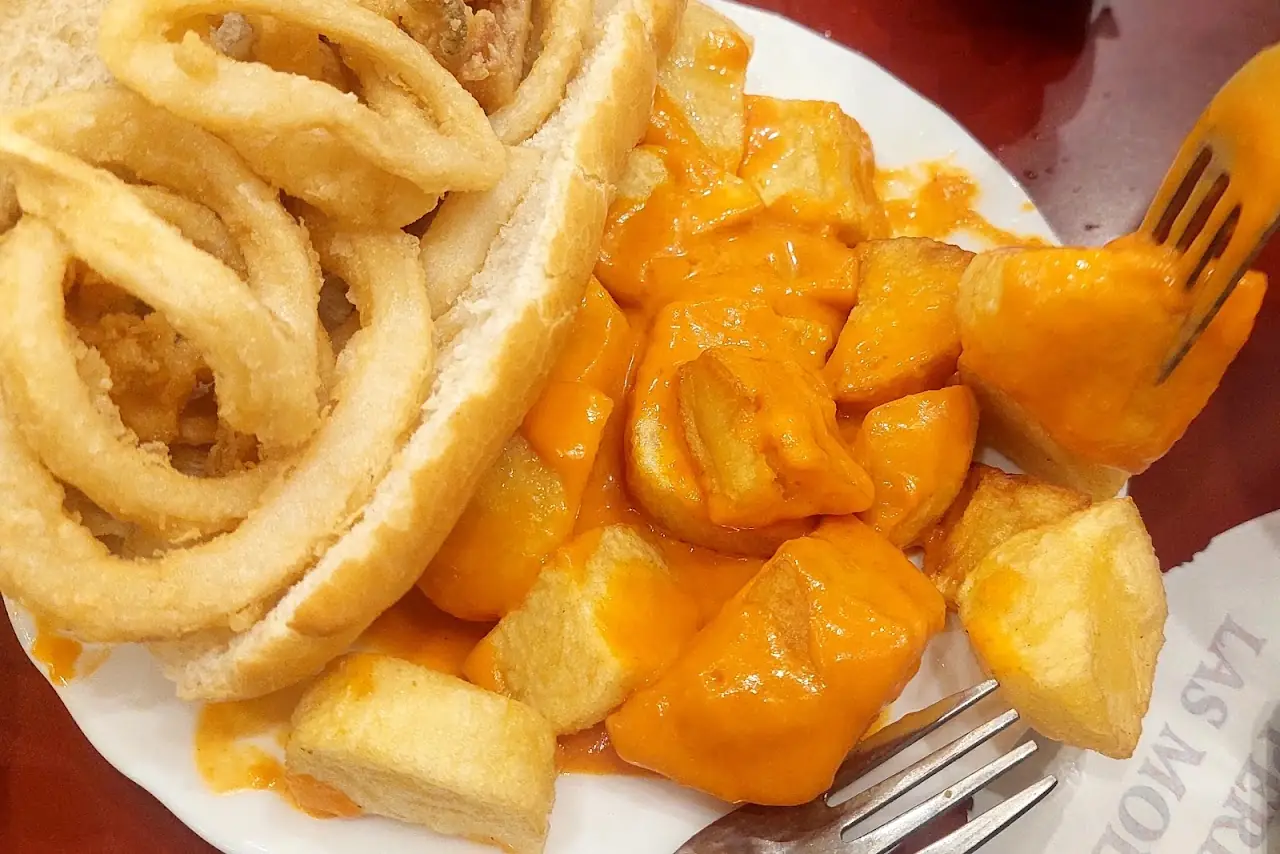 A calamari sandwich beside a plate of patatas bravas in spicy sauce