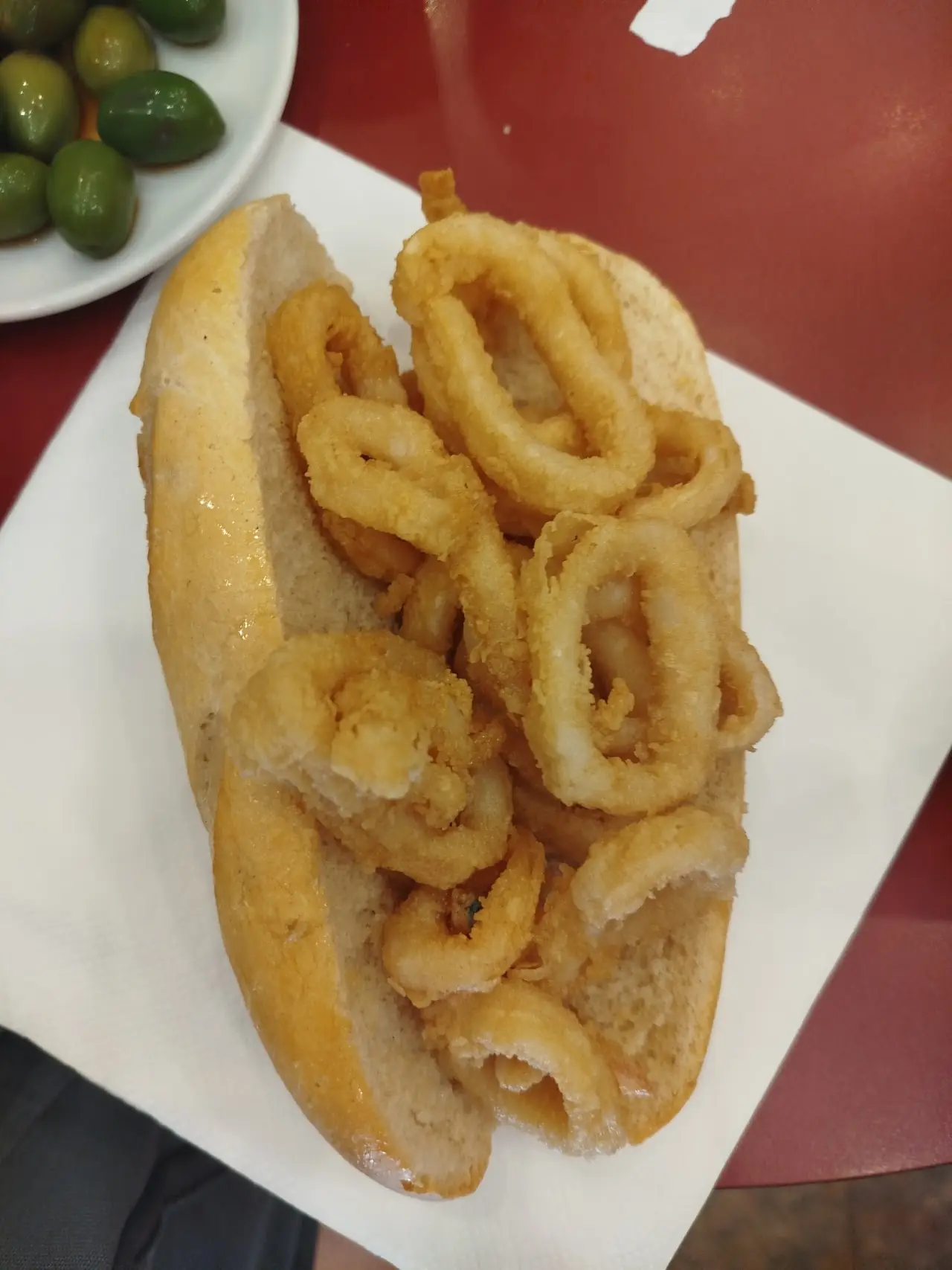 A calamari sandwich on a paper napkin with olives alongside