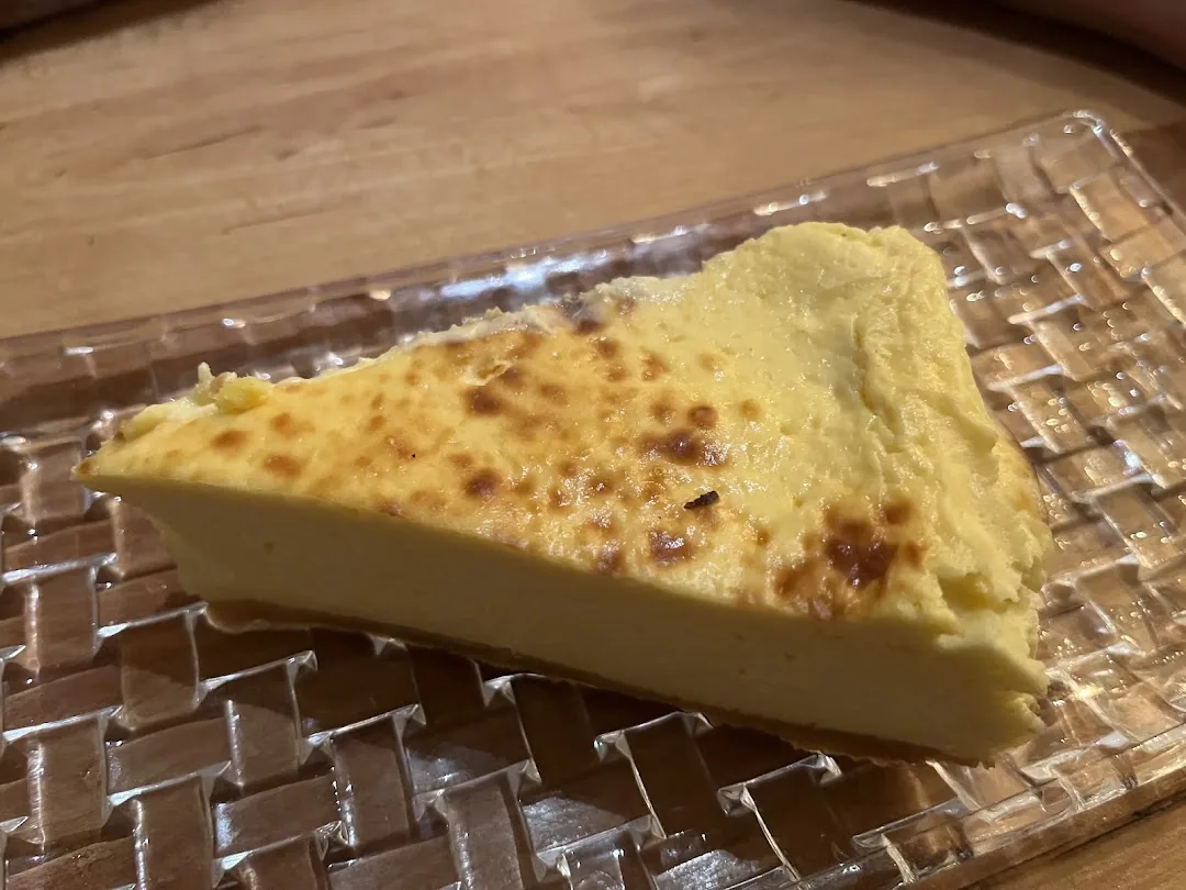 A triangular slice of golden, torch-browned baked cheesecake on a textured glass plate