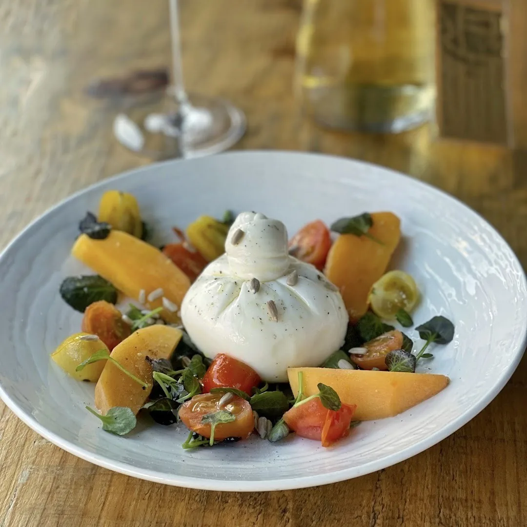 A white bowl of burrata with fruit, tomato and tortellini