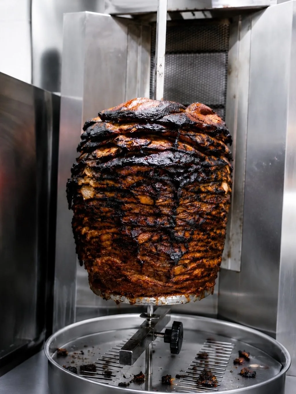 A tall spit of stacked marinated meat turning on a rotisserie