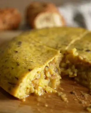 Close-up of a sliced Spanish tortilla on a wooden board with bread rolls in the background