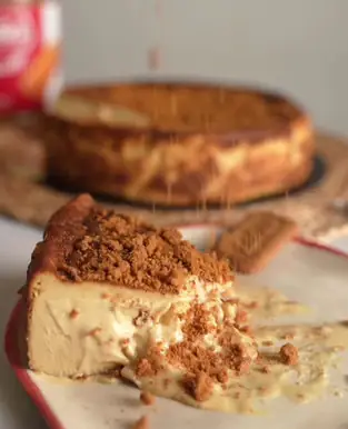 Slice of biscuit-crust cheesecake with caramel drizzle and a cookie garnish, whole cake in the background