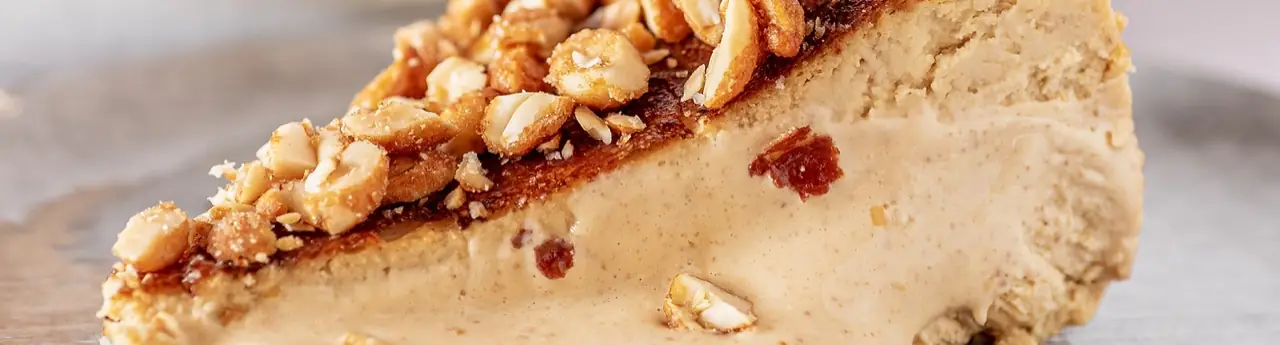 Close-up slice of peanut butter cheesecake topped with chopped peanuts and a jam swirl