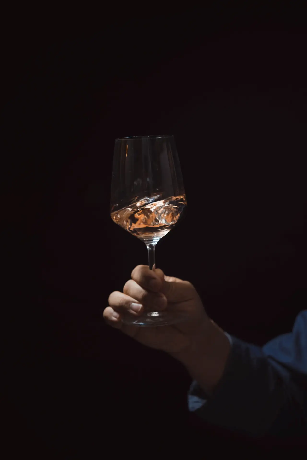 Hand holding a glass of rose wine against a dark background