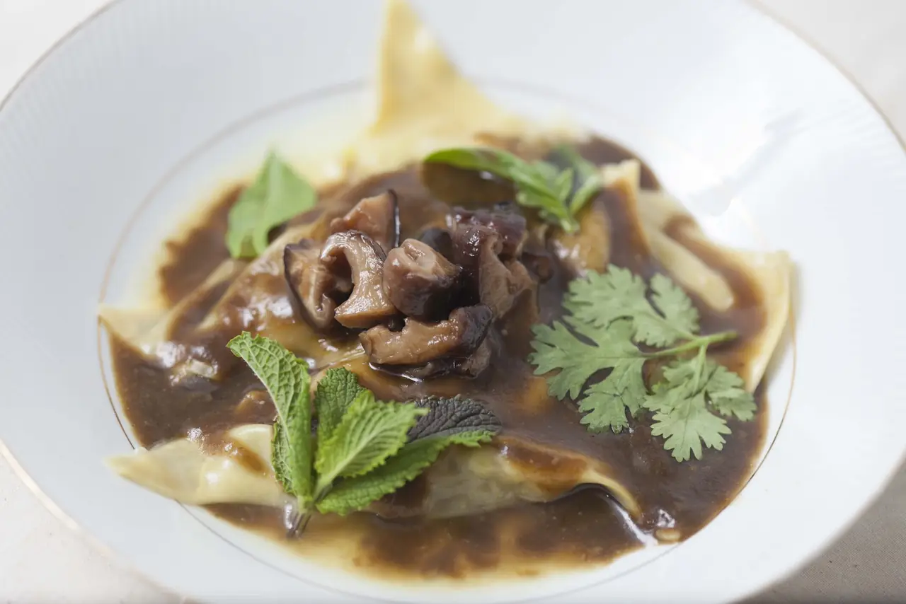 Pasta parcel in mushroom sauce garnished with mint and coriander leaves on a white plate