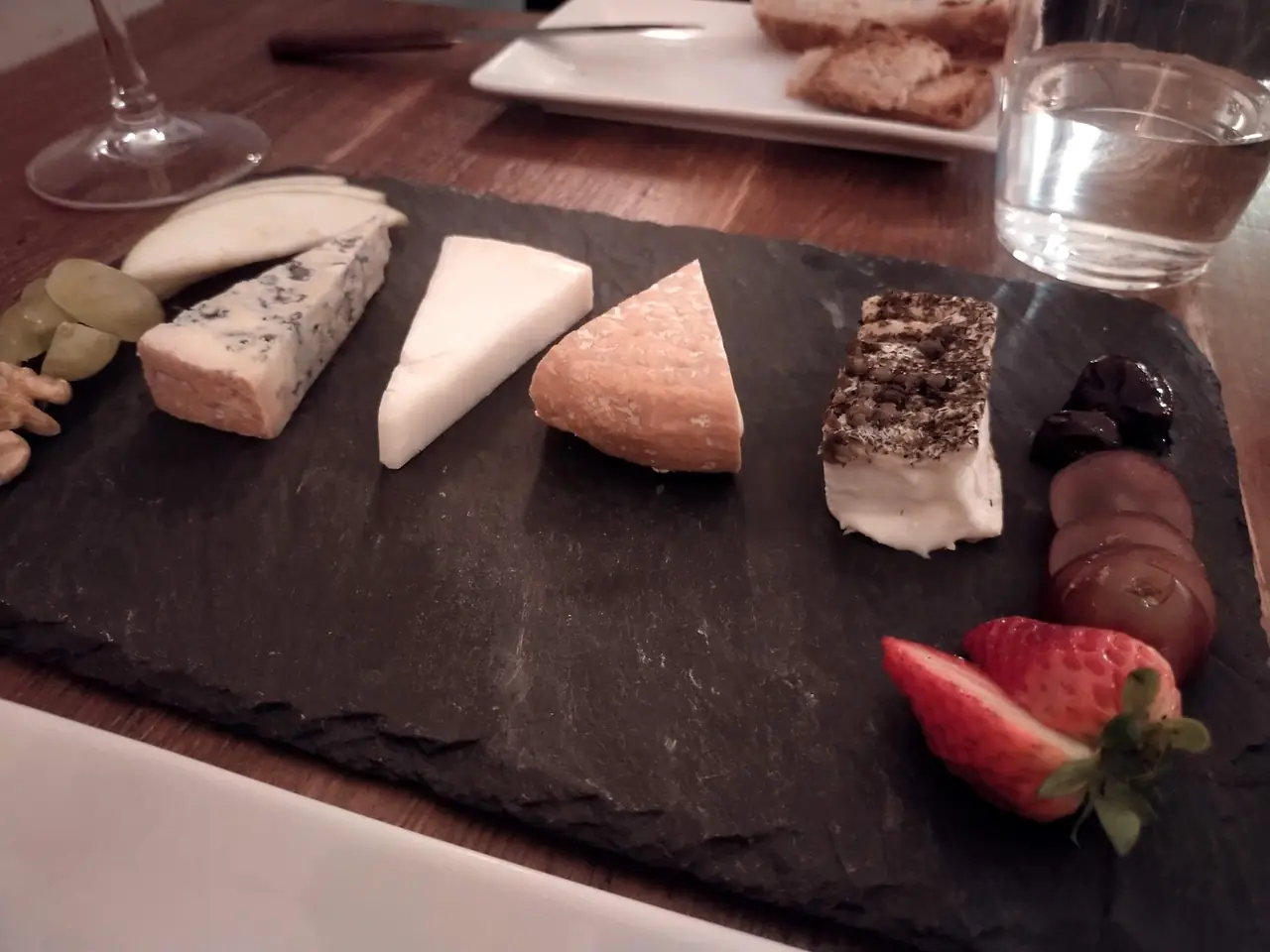 Cheese board with five cheese wedges, walnuts, grapes, strawberry and dried fruit on a slate