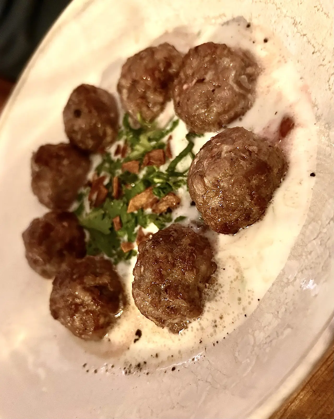 Meatballs in cream sauce with chopped parsley and fried garlic chips on a plate