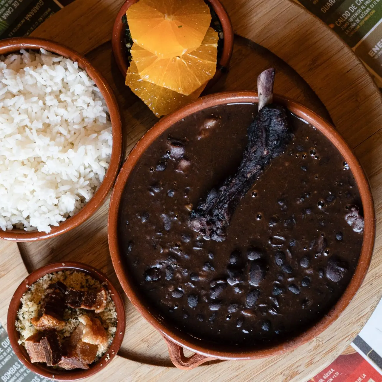 Feijoada with black beans and smoked meat, served with white rice, orange slices, farofa, and crackling in clay bowls, La Carioca