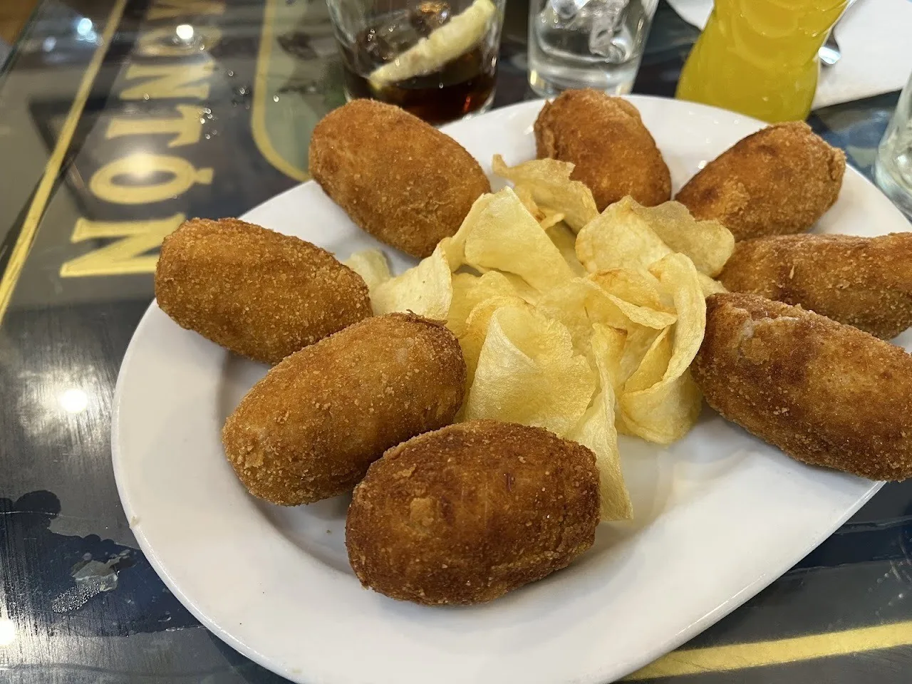 Golden breaded croquetas on a white plate with potato crisps